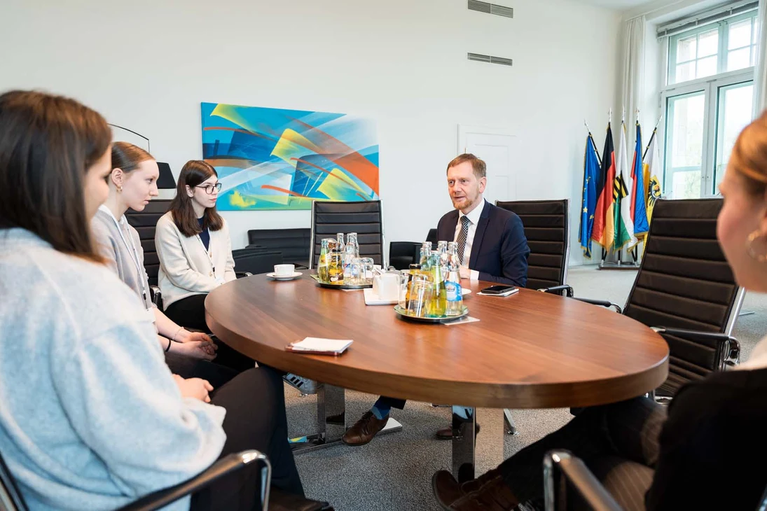 Vier Jugendliche und ein Mann sitzen an einem ovalen Tisch.