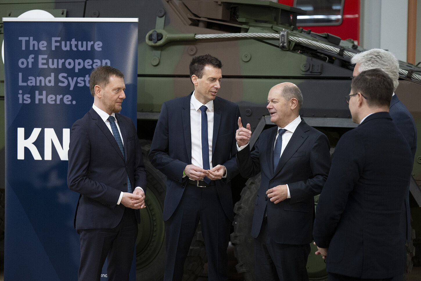 Männer stehen vor einem Panzerfahrzeug.