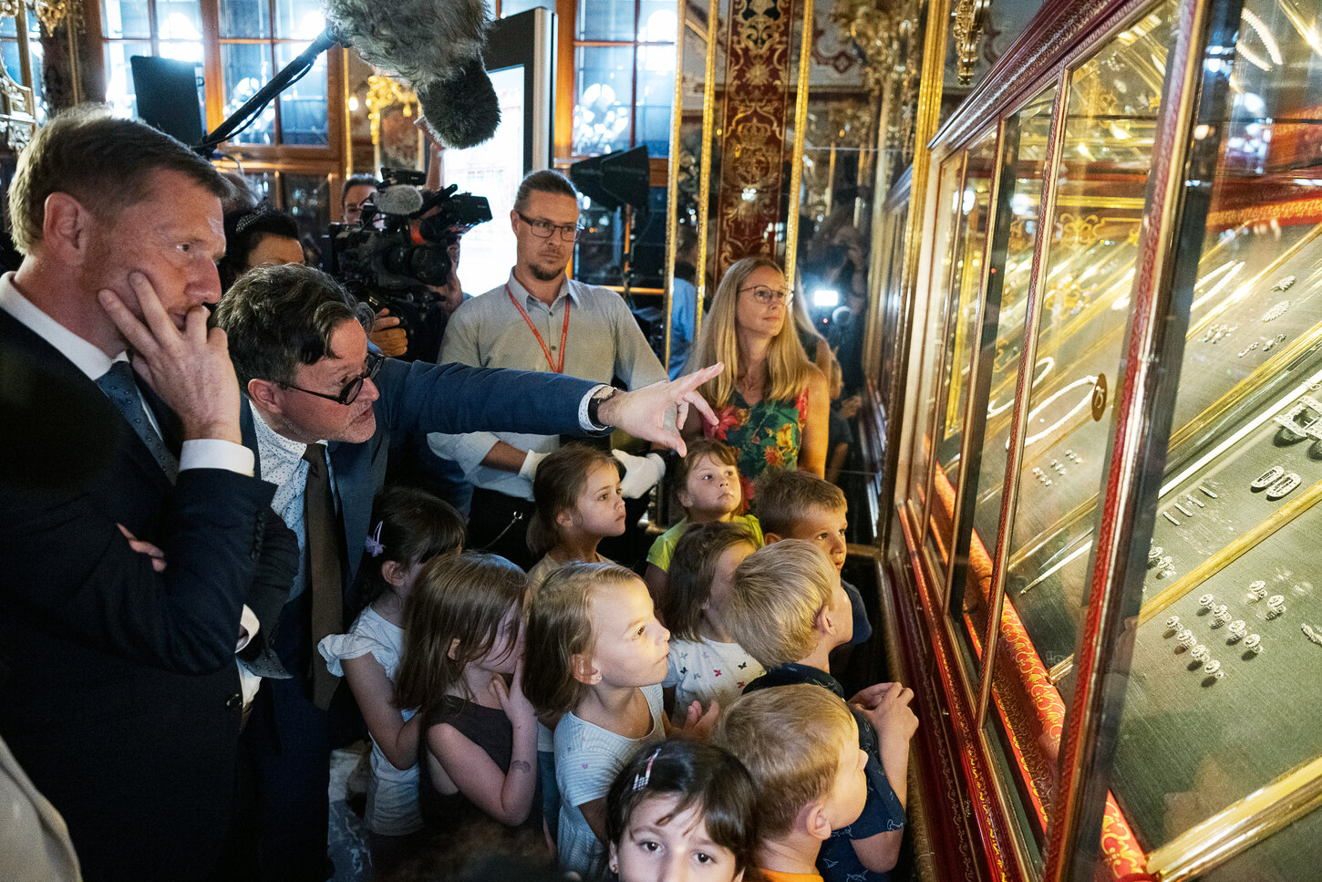 Ein Mann zeigt Kindern Schmuckstücke in einer Vitrine.