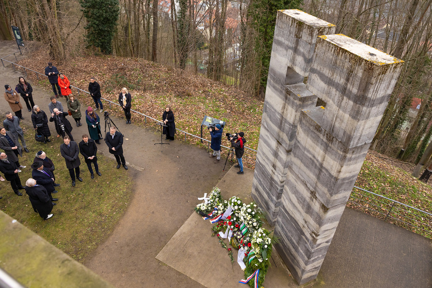 Männer und Frauen stehen andächtig vor einem großen Gedenkstein.